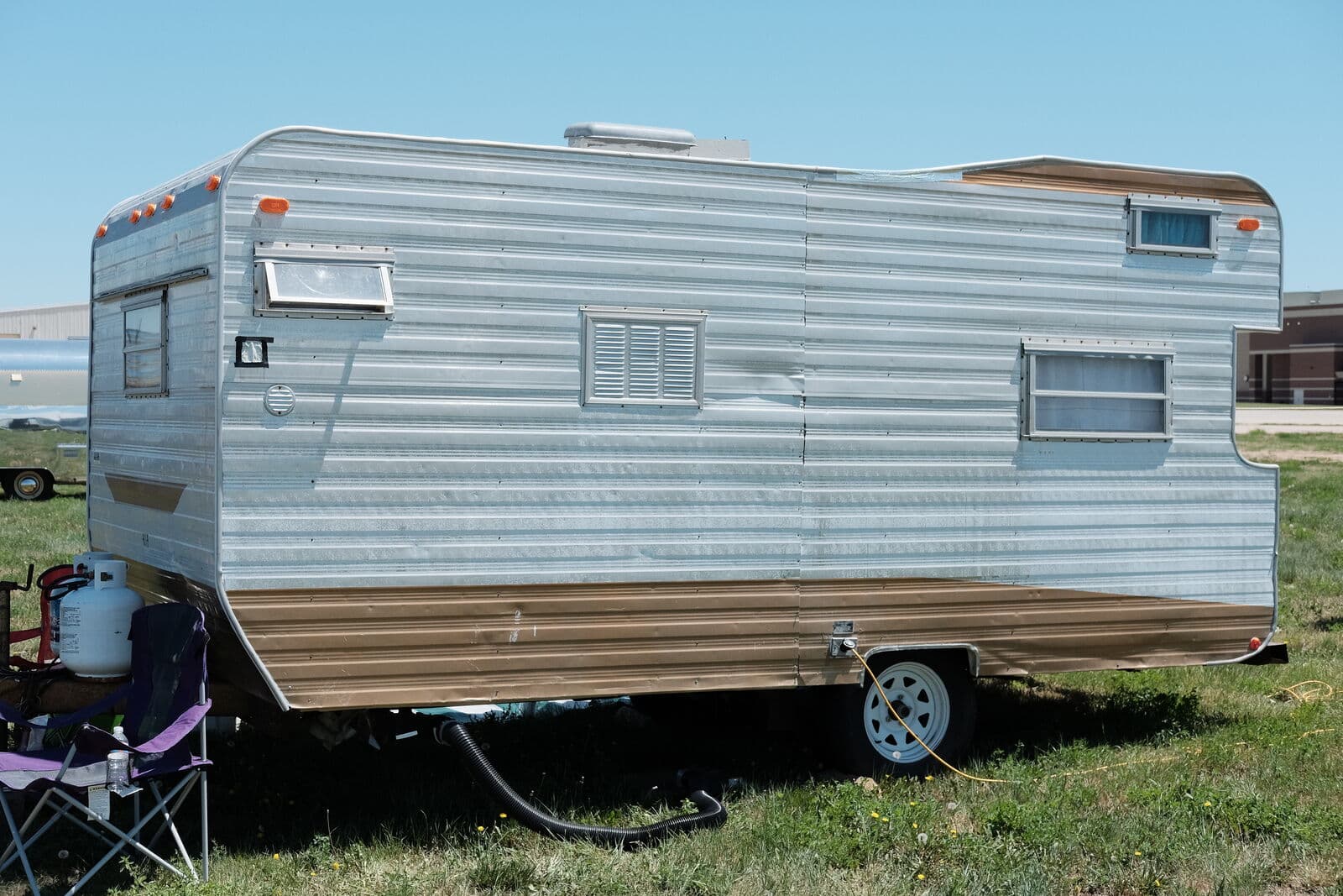 Vintage aluminum travel trailer parked on a grassy field under a clear blue sky.