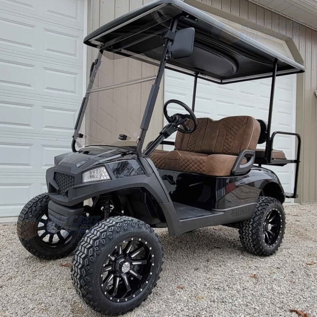 Black lifted golf cart with brown seats and off-road tires parked in front of a garage.
