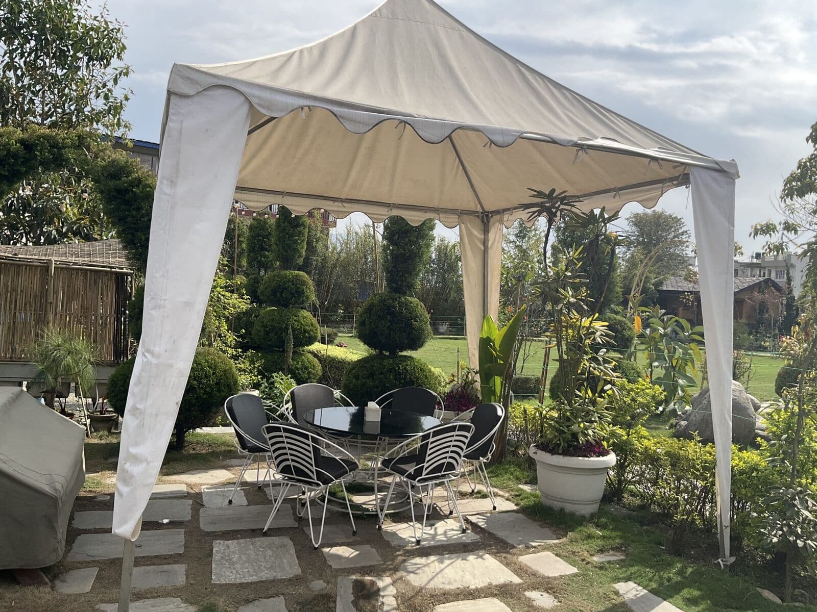 Patio table and chairs under a white canopy on a stone patio in a green garden.